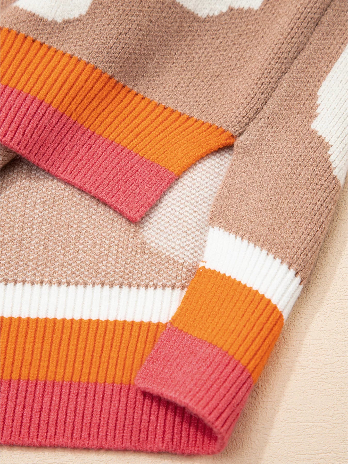 Baggy sweater in tan with a floral pattern and striped cuffs in pink, orange, and white.