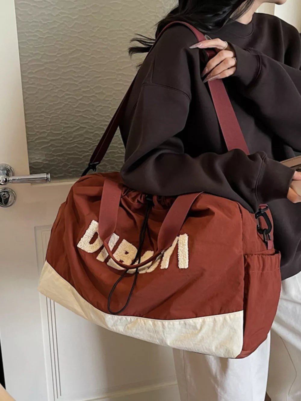 Chic color-blocked travel bag in rust with cream bottom and white textured lettering.