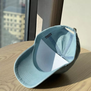 Light blue baseball cap with adjustable strap and embroidered letter detail.