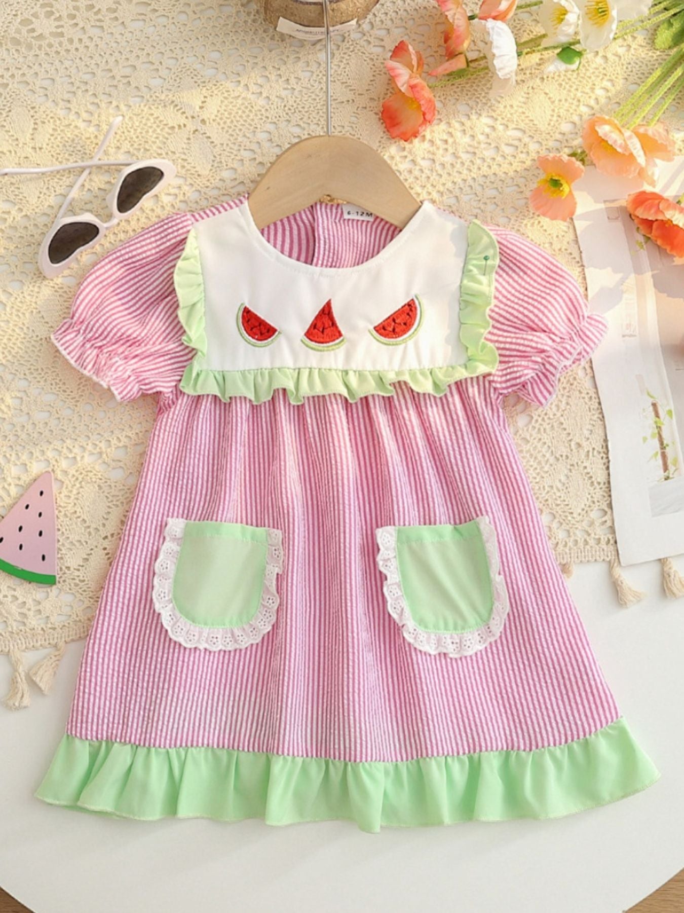Baby dress in pink stripes with watermelon embroidery, green trim, and pockets.