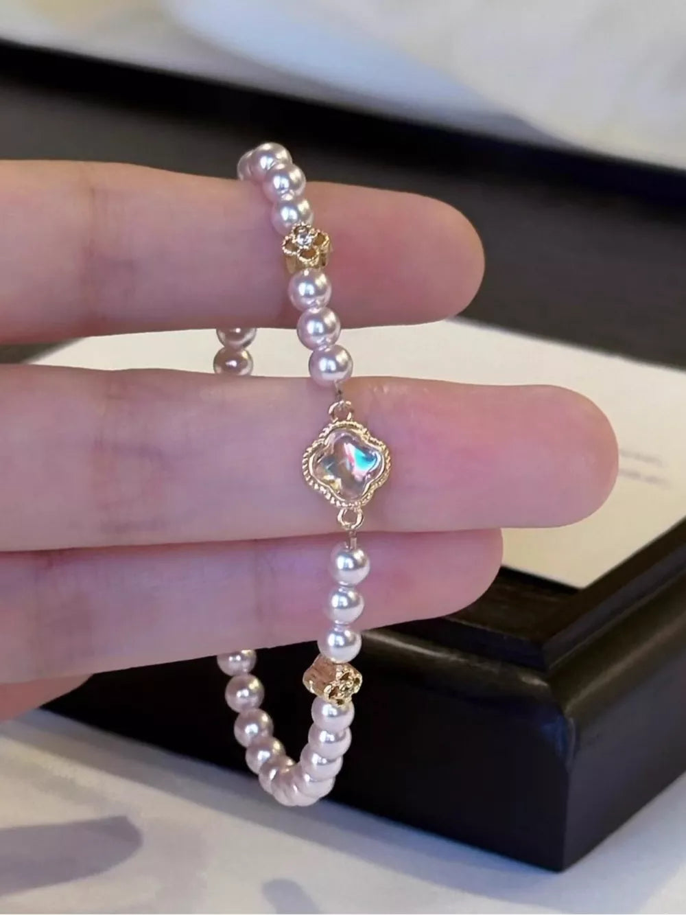 Delicate pearl bracelet with gold clover charm and iridescent center detail.