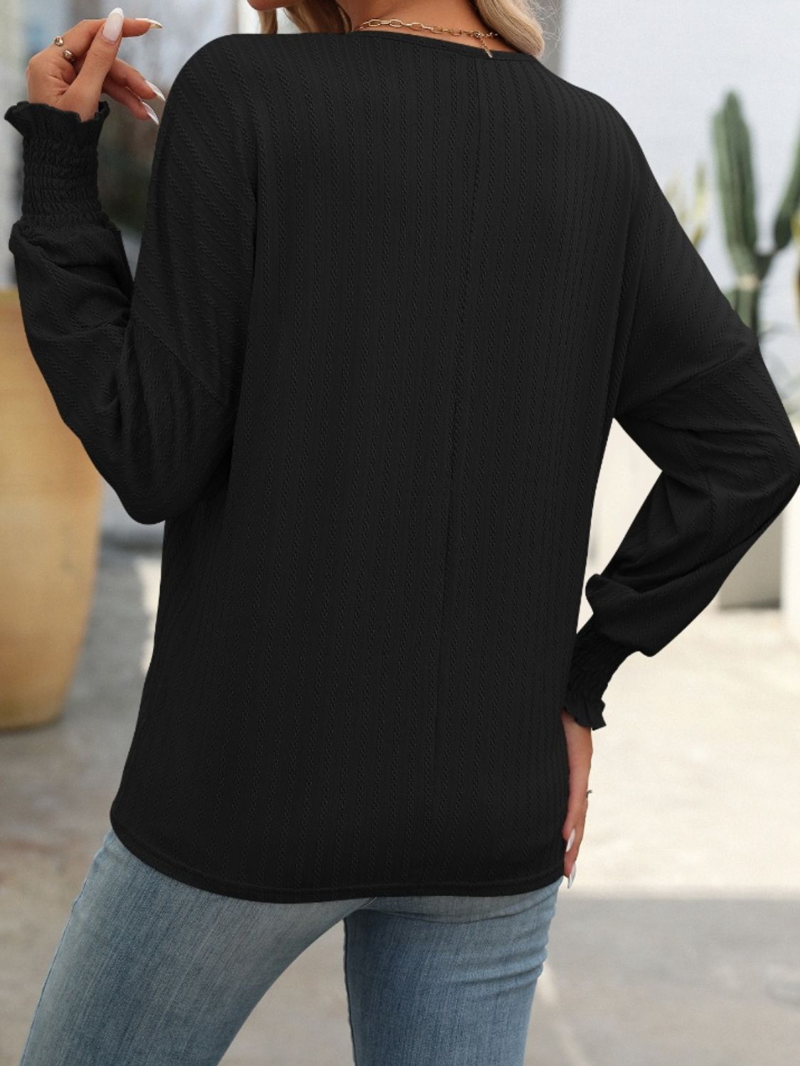 Black textured blouson top with smocked cuffs and long sleeves.