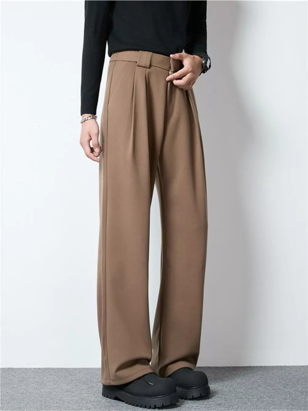 Men's dark brown wide-leg pleated trousers with a relaxed fit and a buckle detail.