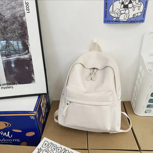 White minimalist leather backpack with front zip pocket and double zipper closure.