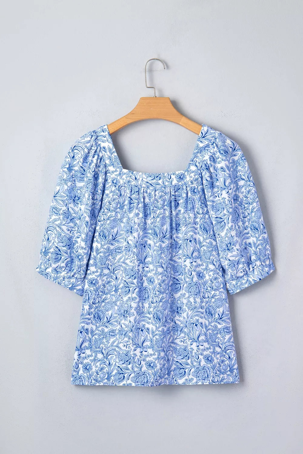 Floral pleated blouse with square neckline and puff sleeves in blue and white print.