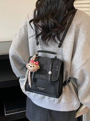 Black mini flap backpack with plush charm and adjustable straps.