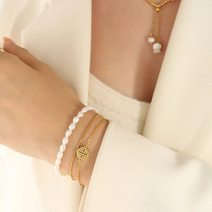 Gold layered bracelet with pearls and a circular charm on a woman's wrist.