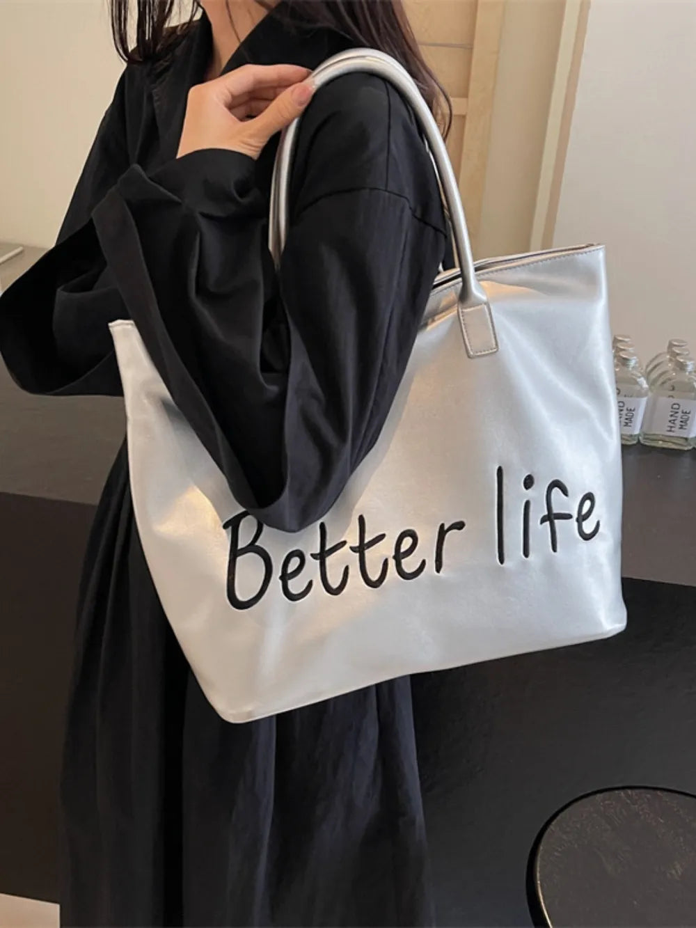 Silver metallic tote bag with black "Better life" graphic and top handles.