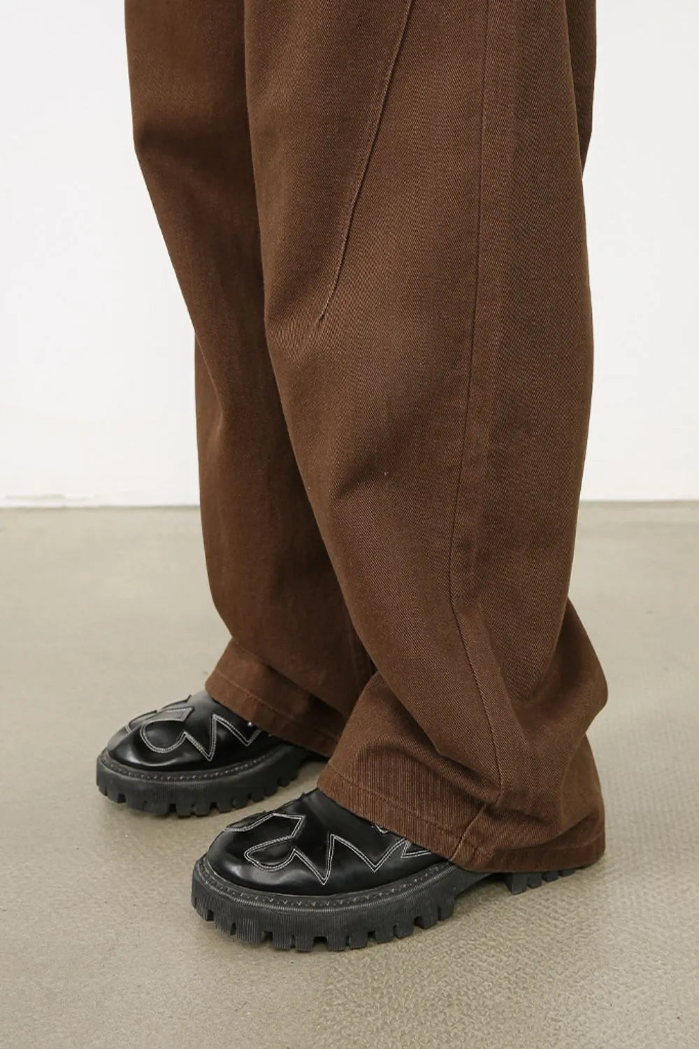 Brown wide-leg denim pants with angled seams and visible stitching detail.