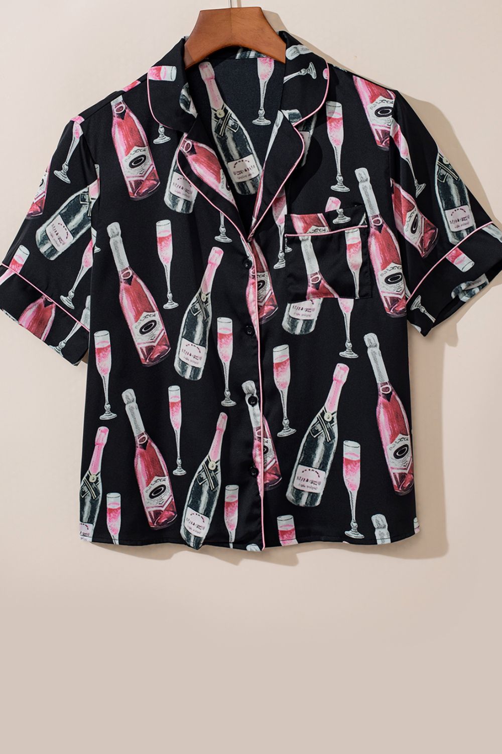 Black silk pajama top with champagne bottle and glass print, pink piping, and short sleeves.