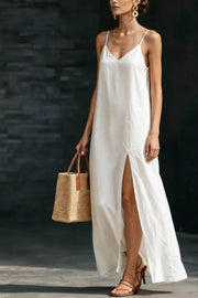 White V-neck maxi dress with spaghetti straps and a high slit, styled with a straw tote bag.