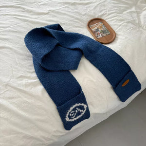 Blue textured knit scarf with pockets featuring white oval logo detail and a brown brand tag.