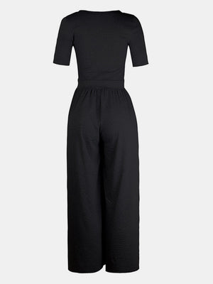 Black textured wide-leg maternity jumpsuit with short sleeves and a subtle elastic waist.