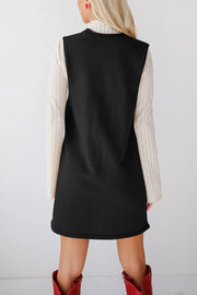 Black knit sweater dress with a deep V-neck, layered over a cream ribbed long-sleeve top.