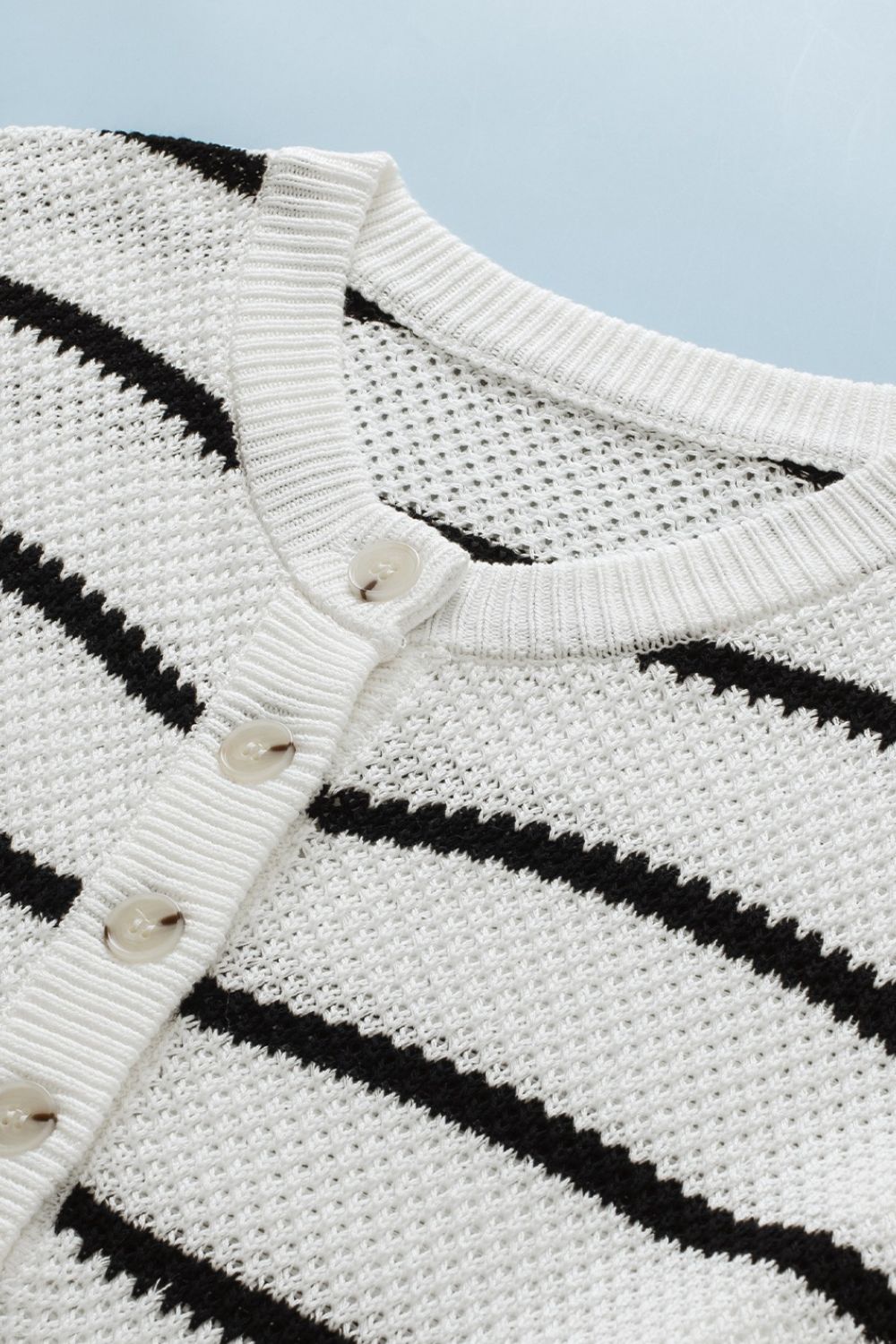 Button-down stripe knit pullover sweater in white with black stripes and round neckline.