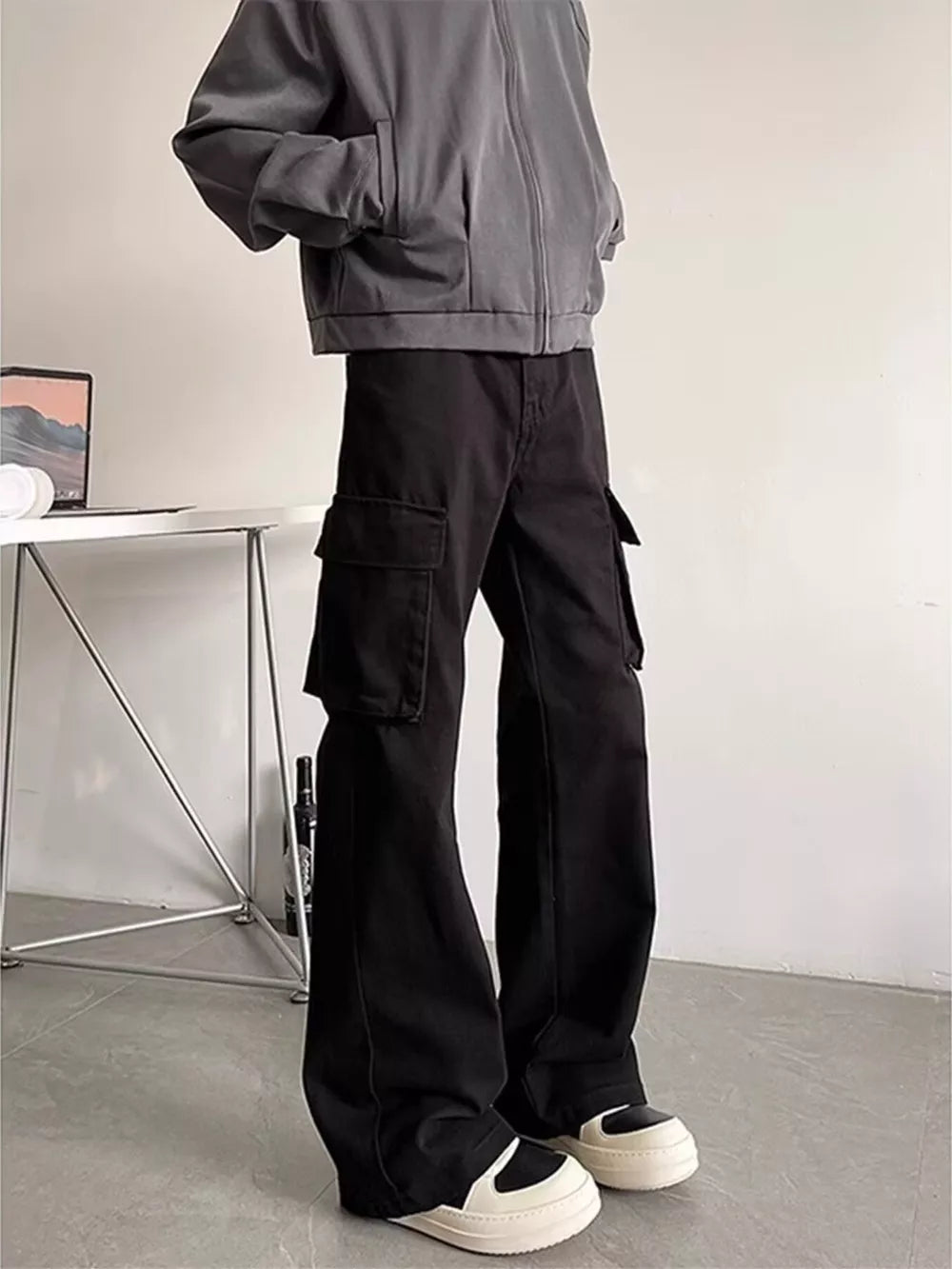 Black cargo pants with large side pockets, styled with a grey jacket and sneakers.