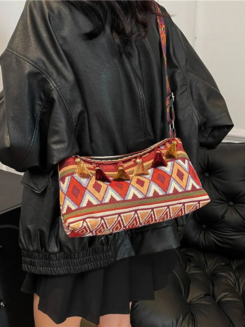 Geometric embroidered shoulder bag with tassels and colorful woven pattern.