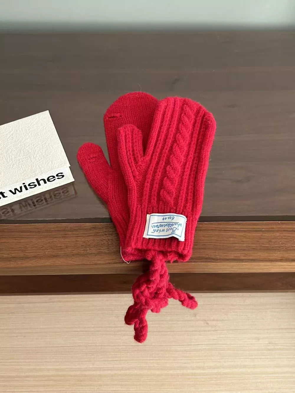 Red cable knit acrylic mittens with a braided detail and a knotted string.