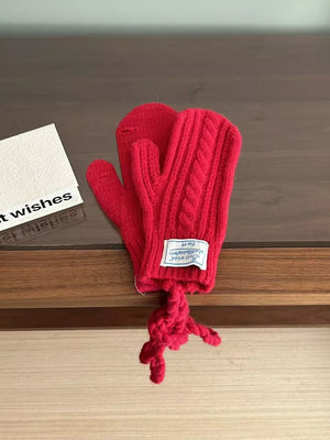 Red cable knit acrylic mittens with a braided detail and a knotted string.
