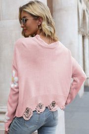 Pink acrylic knit sweater with distressed hem and daisy appliqué on sleeve.
