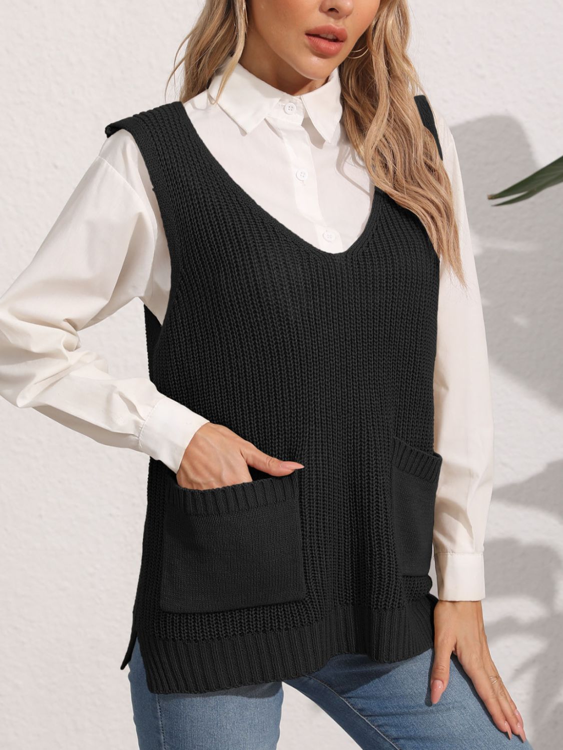 Black oversized knit vest with V-neck and patch pockets, styled over a white shirt.