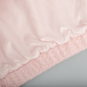 Blush pink bouclé bomber jacket with a smooth satin lining and rounded neckline detail.