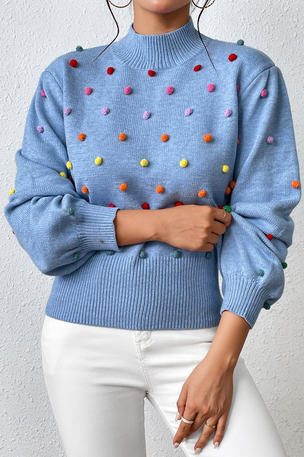 Blue blouson knit sweater with multicolor pom-pom embellishments and mock neck.