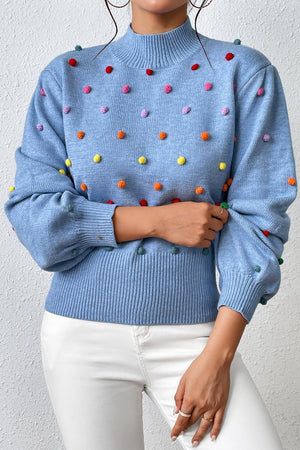 Blue blouson knit sweater with multicolor pom-pom embellishments and mock neck.