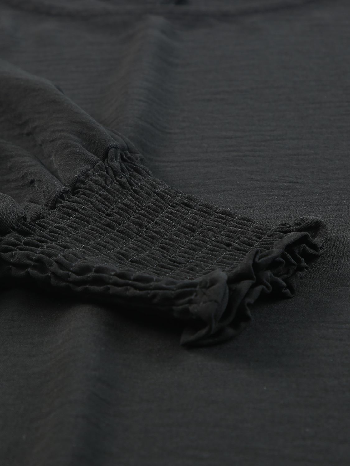 Black textured sleeve blouse with elastic smocked cuffs and ruffled hem detail.