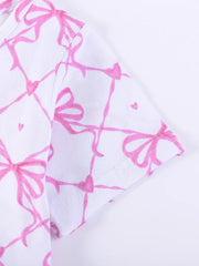 Baby dress with pink bow and heart print on white cotton fabric.