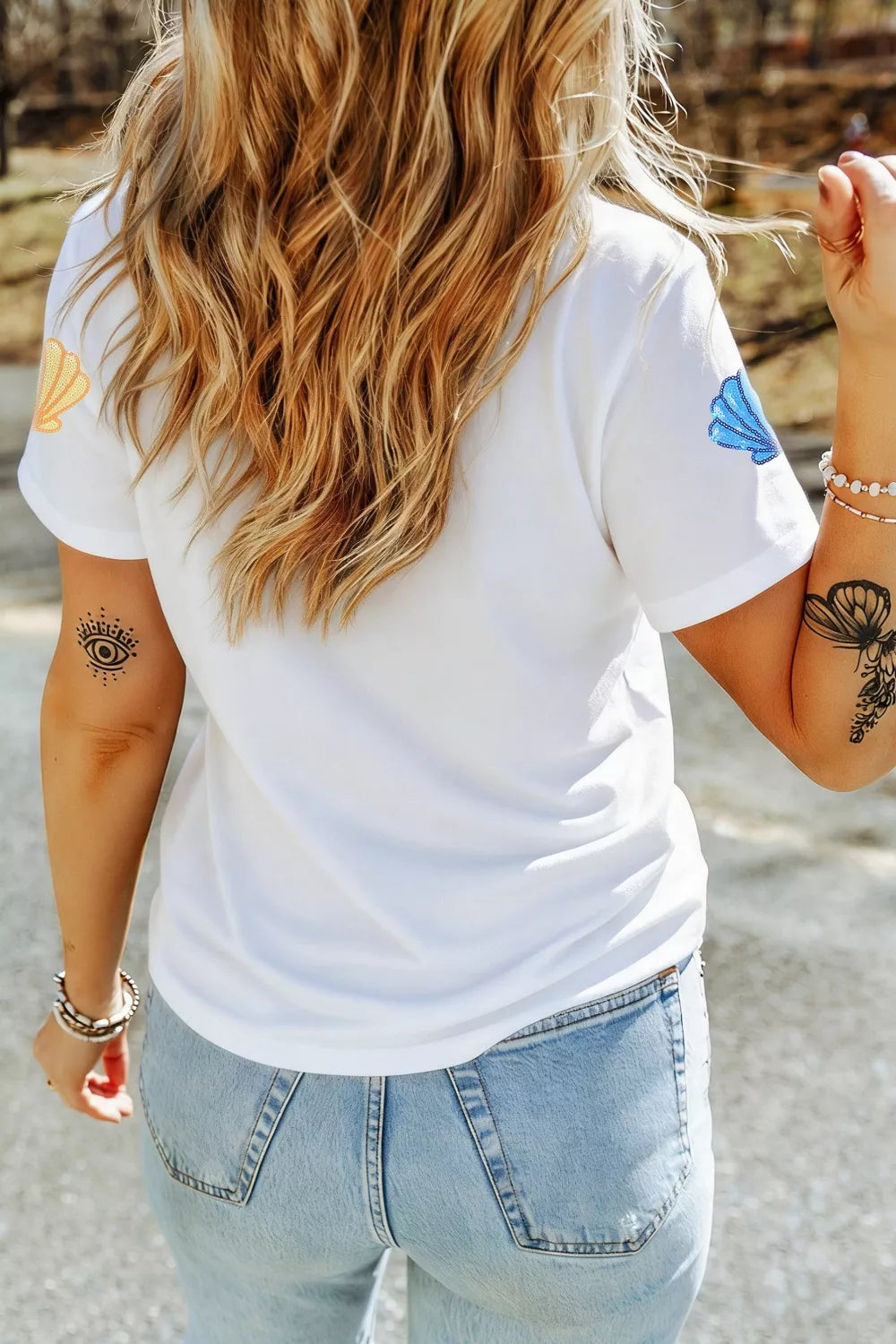 White polyester t-shirt with sequin shell graphics on sleeves and eye tattoo.