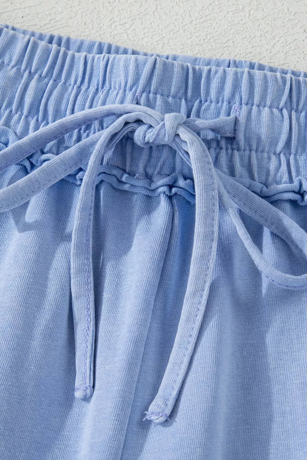 Light blue cotton drawstring shorts with ruffled waist detail and tie.