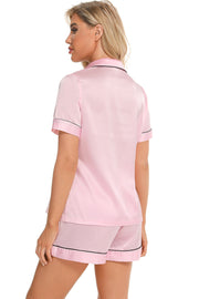 Pink satin pajama set with black piping detail, short sleeves and shorts.