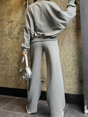 Gray zip-up sweatshirt with cinched waist and wide-leg pants, styled with a silver handbag.