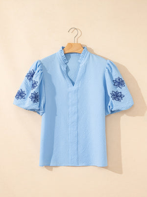 Light blue textured blouse with embroidered puff sleeves and ruffled neckline