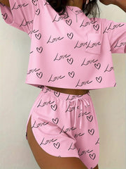 Pink pajama set with all-over black love heart and script print, featuring a cropped tee with pocket and drawstring shorts.