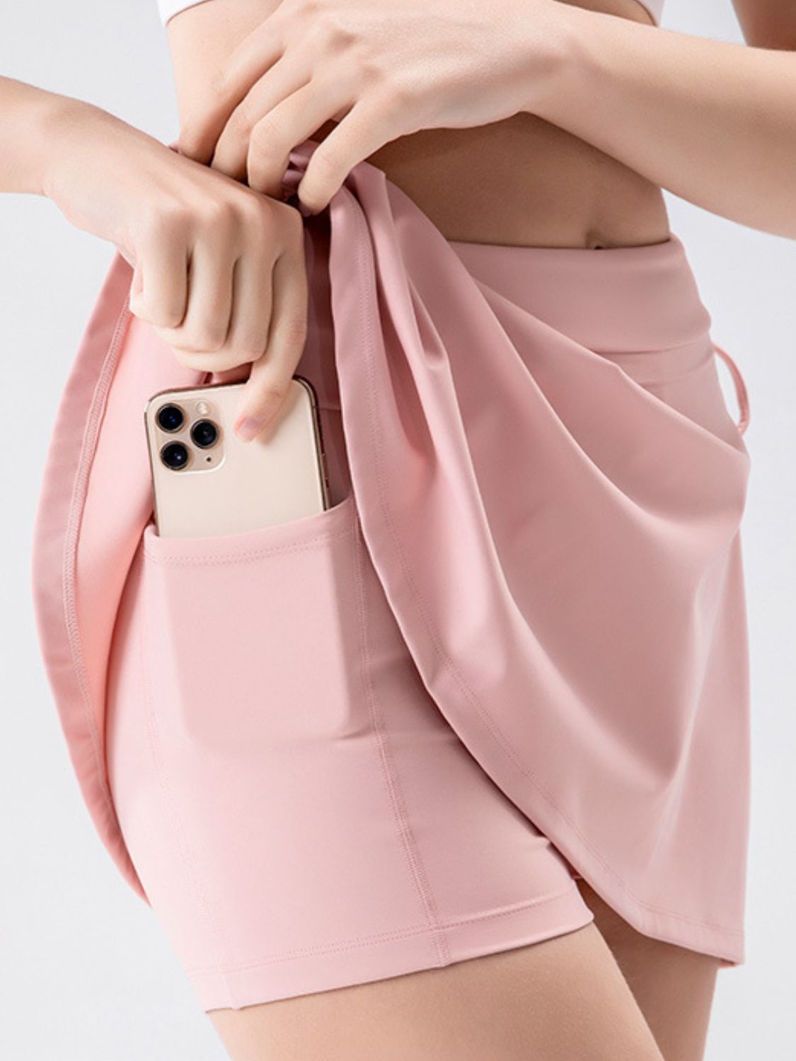 Blush pink wrap skort with side tie detail and pocket holding a phone.