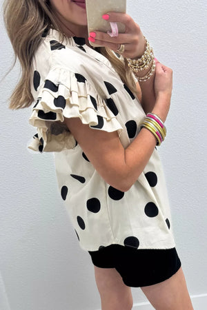 Cream cotton shirt with black polka dots, V-neck, and ruffled short sleeves.