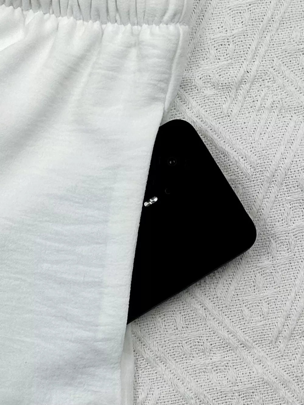 White relaxed fit maternity pants with elastic waistband and side pocket holding a phone.