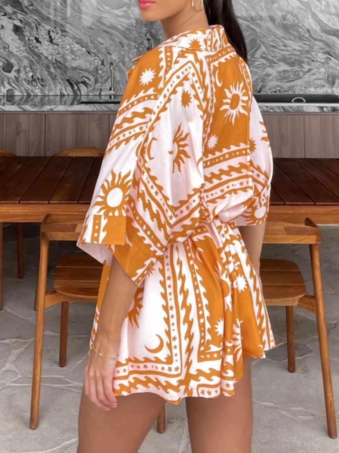 Wrap romper in gold with celestial print, short sleeves, and adjustable fit.