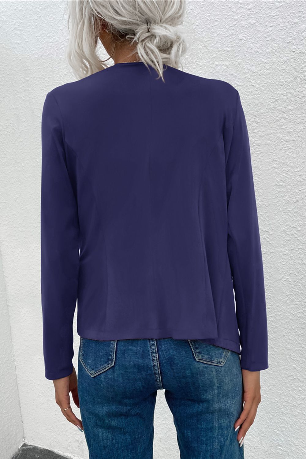 Dark blue jacket with long sleeves and a draped front, styled with jeans.