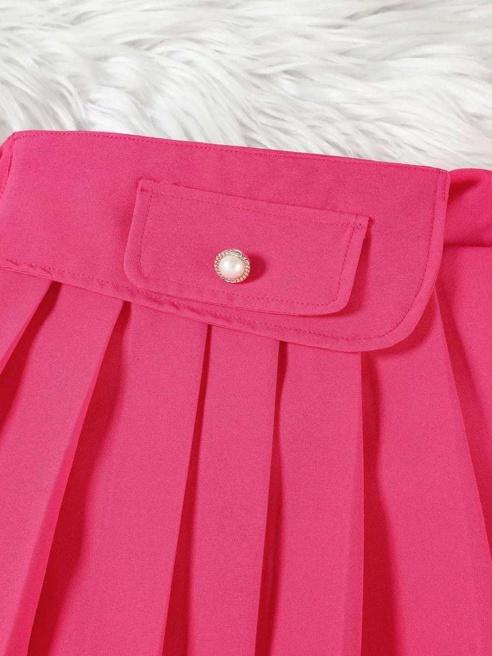 Pink baby skirt with pleated detail and decorative button on pocket.