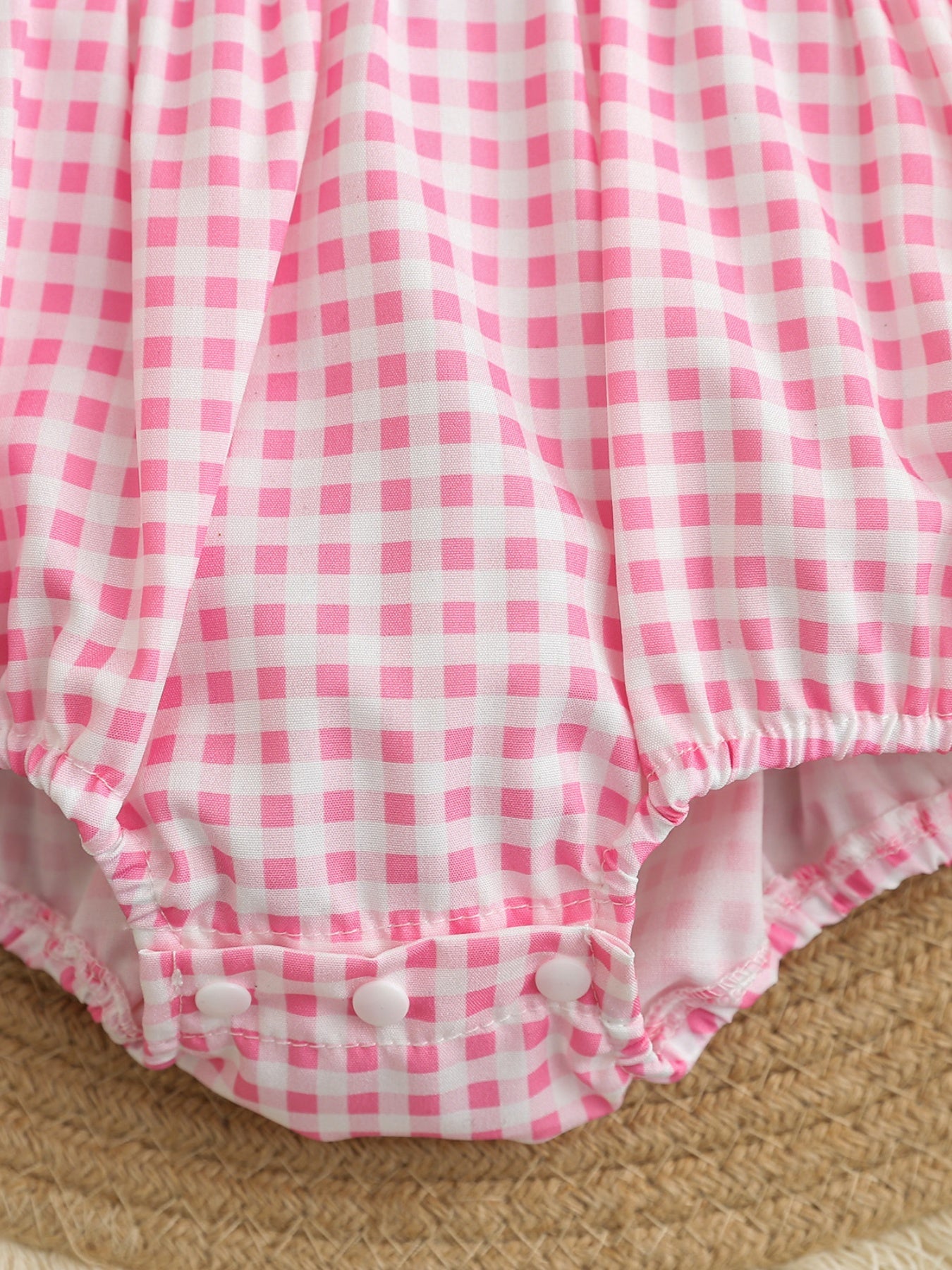 Baby pink gingham one-piece with snap closure and elastic leg openings.