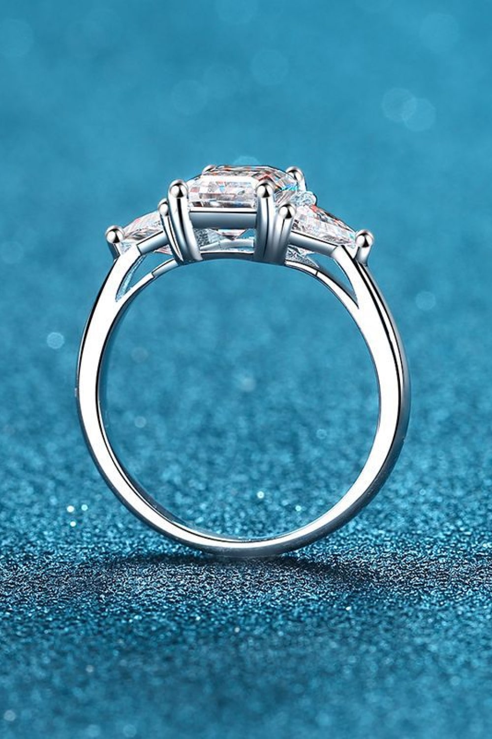 Silver trilogy ring with a central emerald-cut stone and two trapezoid side stones.