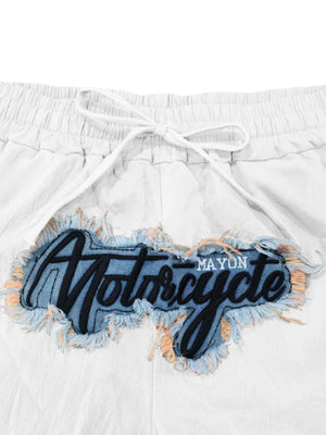 White drawstring sweatpants with a distressed denim patch featuring black embroidered "Motorcycle" text.