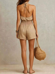 Backless halter romper in beige with smocked waist and short legs.