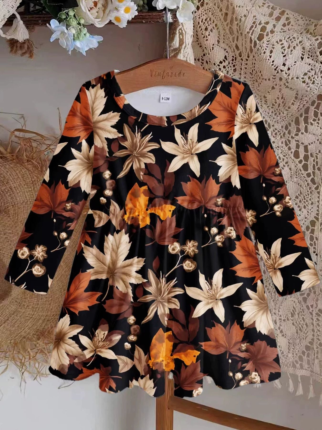 Baby dress with long sleeves and autumn leaves print on black polyester fabric.