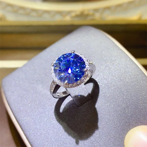 Silver halo cocktail ring with large blue stone and small clear stones on band.