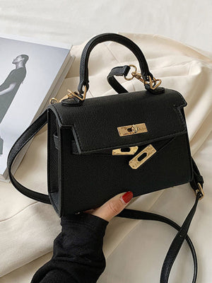 Black mini crossbody bag in textured pu leather with gold hardware and top handle.