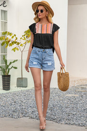 Black blouse with embroidered yoke and ruffle sleeves, paired with denim shorts.